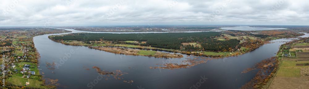Wide aerial view of a river curving through a landscape with forests, fields, and residential areas. Overcast sky adds a muted tone to the scene. Wide aerial view of a river curving through a landscape with forests, fields, and residential areas. Overcast sky adds a muted tone to the scene.