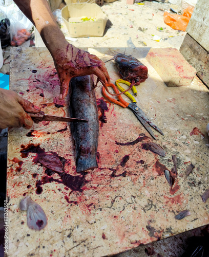 Cutting fish on the table. Fish market. A man cleans the entrails and cuts a catfish into pieces. Day. Autumn. Egypt.