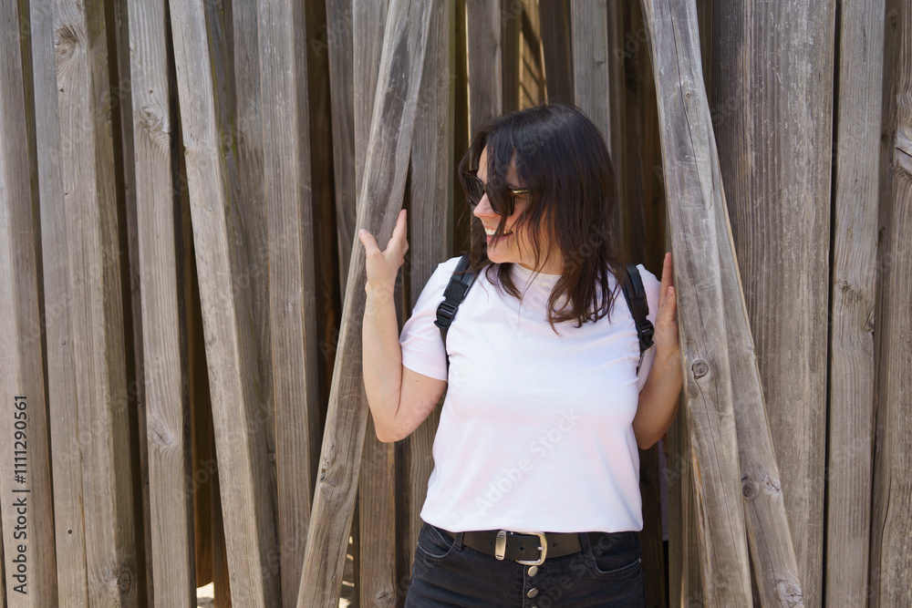 Fototapeta premium Beautiful smiling dark-haired girl in a white T-shirt and with a backpack on her shoulders in the summer on a trip. Pedestrian wanderung concept