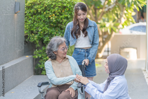 asian senior woman on wheelchair hands holding a female physiotherapist in hijab,a daughter standing behind her,health care worker empowering patient or better health