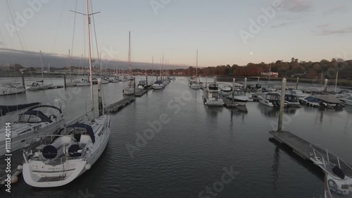 Aerial drone flying over yachts and sailboats moored in marina under sky at dusk in Swanwick, England. Calm water reflects boats and soft light, creating a serene evening scene. photo