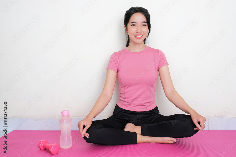 Fototapeta premium A woman sitting on yoga mat doing exercise with happy expression