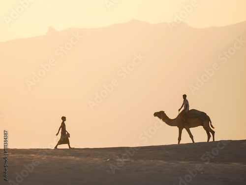 Silhouetted Camel Rider at Sunset in a Serene Desert Landscape photo