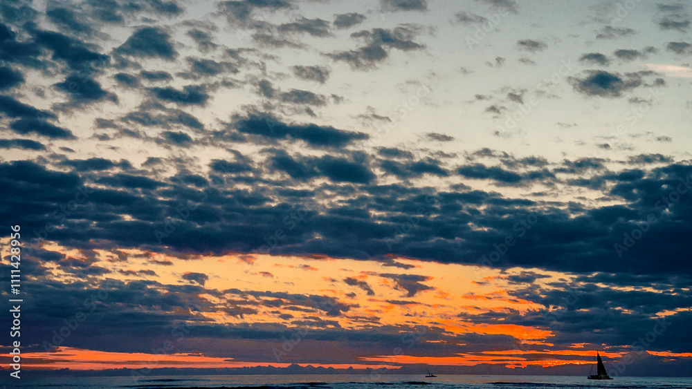 Fototapeta premium Dramatic Ocean Sunset with Vibrant Clouds and a Silhouetted Sailboat