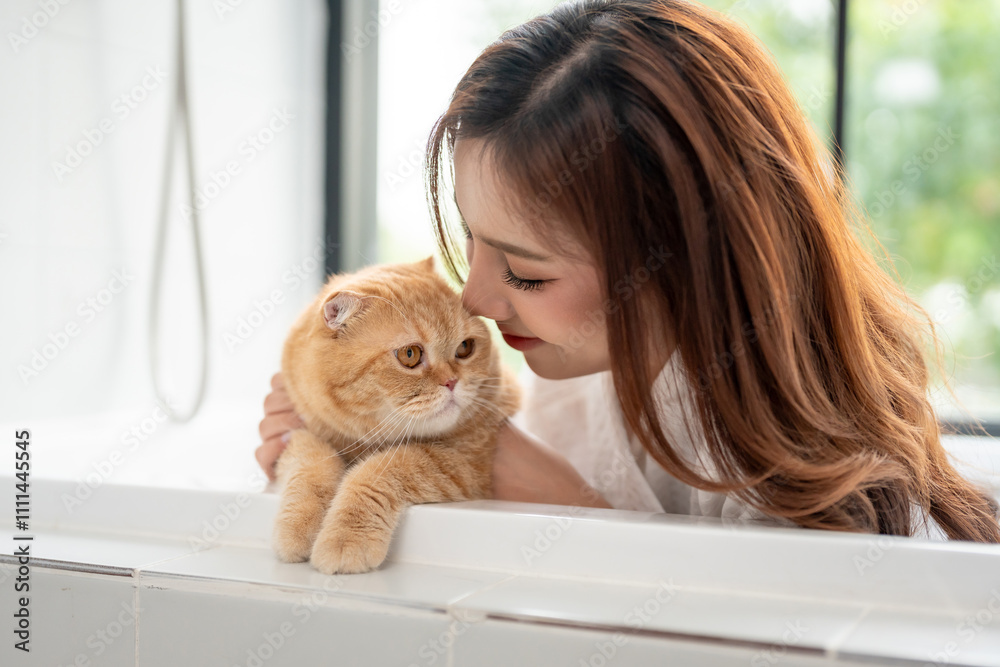 Asian young woman sitting in bathtub with her domestic cat in bathroom. Asian young woman sitting in bathtub with her domestic cat in bathroom.