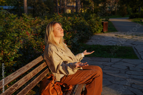 Young woman sitting on park bench and enjoying the sun rays, relaxing with eyes closed             