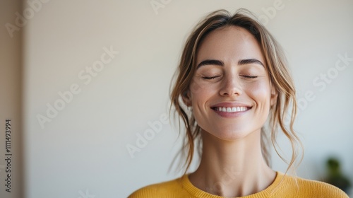 Smiling woman with closed eyes, radiating joy and tranquility, dressed in a yellow sweater against a neutral background.