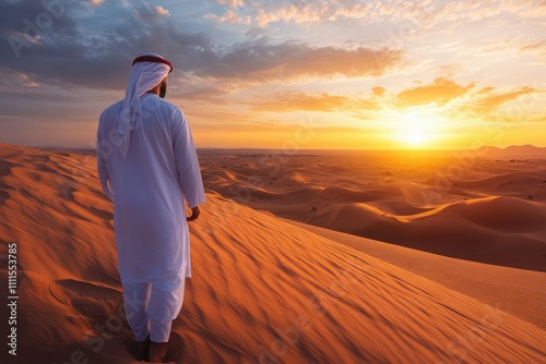 A man in traditional Emirati attire contemplates a breathtaking desert sunset.