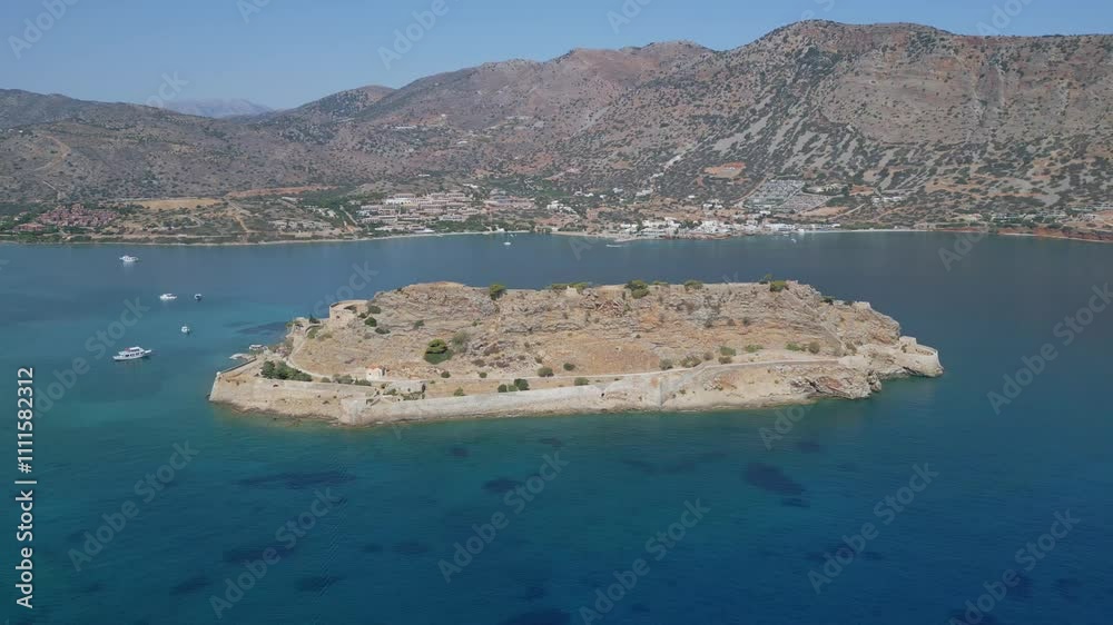 A sweeping panoramic view of Spinalonga Island in the summer, framed by its serene coastline and vibrant blue seas A sweeping panoramic view of Spinalonga Island in the summer, framed by its serene coastline and vibrant blue seas