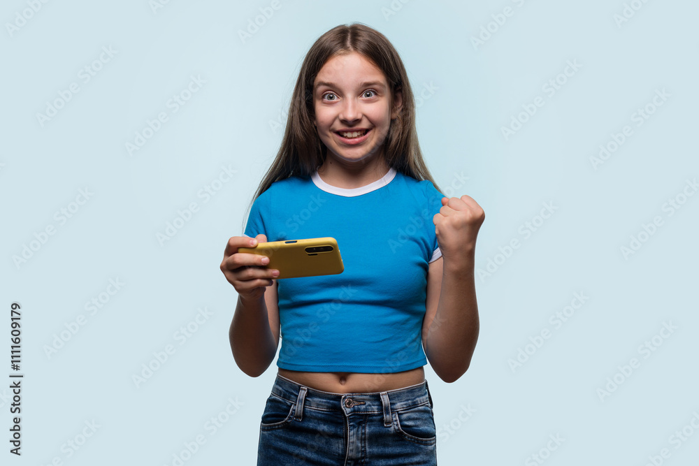A young girl cheering and raising her fist while looking at her yellow smartphone, excited and happy A young girl cheering and raising her fist while looking at her yellow smartphone, excited and happy