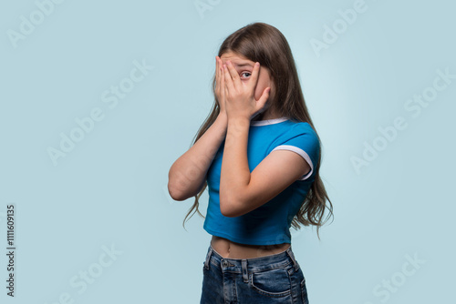 A young girl covering her face with her hands in embarrassment or fear, peeking through her fingers