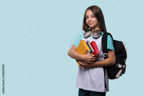 Young girl with a backpack and books, ready for school, wearing headphones around her neck. Teenager in white and light blue raglan