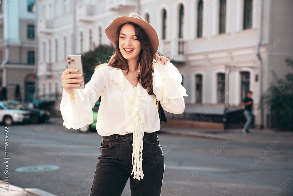 Portrait of young beautiful smiling hipster woman in trendy summer white blouse and jeans. Carefree woman posing in the street in sunny day. Positive model outdoors. Cheerful and happy, take selfie Portrait of young beautiful smiling hipster woman in trendy summer white blouse and jeans. Carefree woman posing in the street in sunny day. Positive model outdoors. Cheerful and happy, take selfie