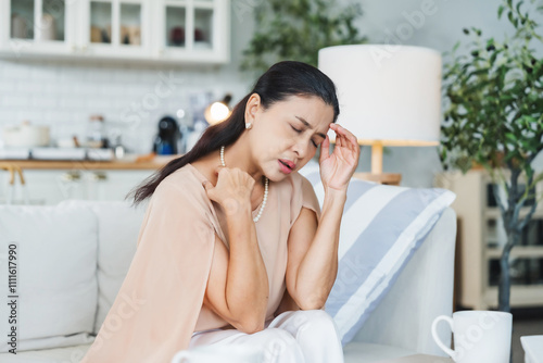 Upset Asian senior woman sitting on sofa, lost in thoughts, feeling lonely, disappointed, alone at home, unhappy, anxious, missing or sad. Senior woman experiencing mental health problems