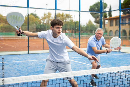 Portrait of sporty young guy playing padel on open court on summer day, ready to hit ball. Sport and active lifestyle concept..