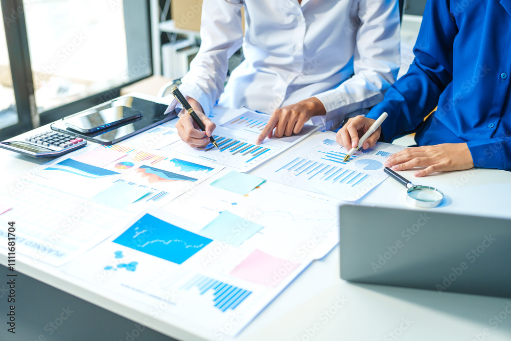 Two Asian business woman working and talking at a table with documents, a graph, and a digital tablet. They are focused on analysis, business planning, and collaborative discussions Two Asian business woman working and talking at a table with documents, a graph, and a digital tablet. They are focused on analysis, business planning, and collaborative discussions