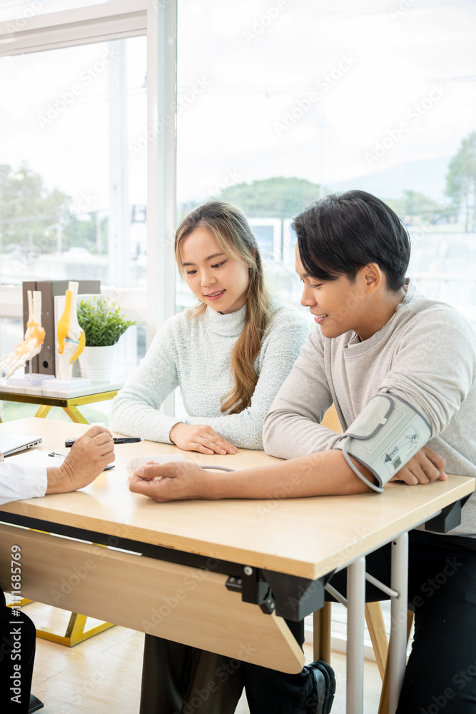 A professional senior Asian female doctor in a uniform having a consultation with a young married couple in the examination room. doctor visit, health care, medical A professional senior Asian female doctor in a uniform having a consultation with a young married couple in the examination room. doctor visit, health care, medical