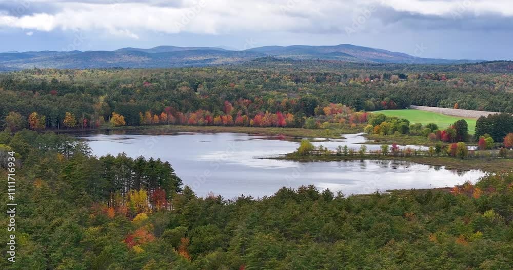 Drone view approaching a still, reflective lake in a lush forest, New Hampshire Drone view approaching a still, reflective lake in a lush forest, New Hampshire