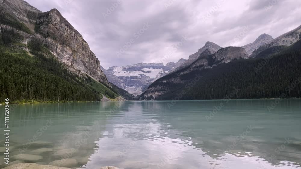 Serene view of Lake Louise turquoise waters reflecting surrounding majestic mountains and glaciers in Banff National Park, Alberta, Canada, Low angle water surface point of view Serene view of Lake Louise turquoise waters reflecting surrounding majestic mountains and glaciers in Banff National Park, Alberta, Canada, Low angle water surface point of view