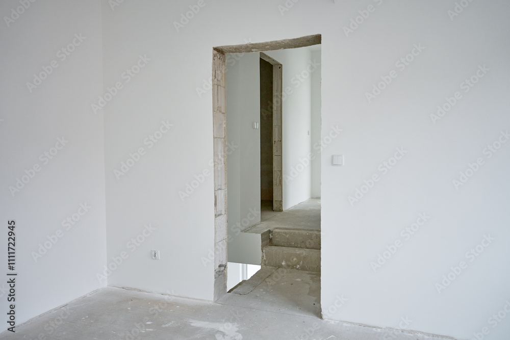 Empty apartment with white walls and concrete floor undergoing renovation. Interior of building under construction Empty apartment with white walls and concrete floor undergoing renovation. Interior of building under construction