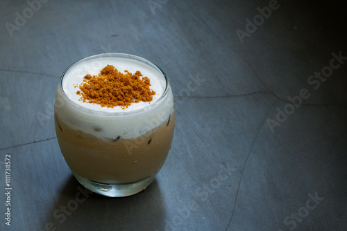 iced sea salt coffee in a curved transparent glass, with brown sugar toppings, placed on concrete surface