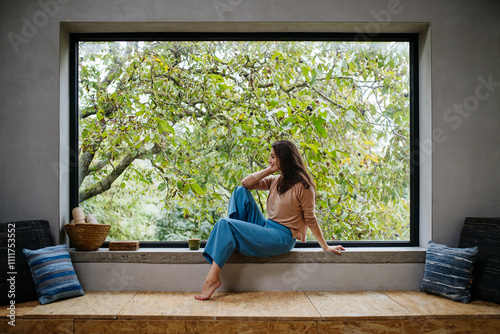 Beautiful woman sitting in front of large window, clean space. photo