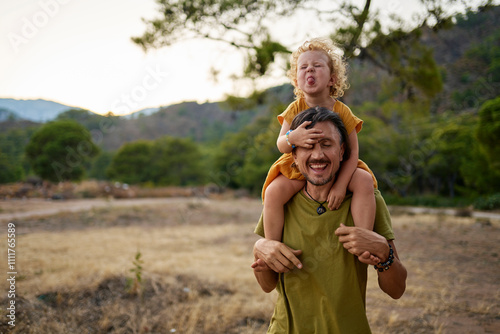 Girl sticking out tongue sitting on father's shoulders photo