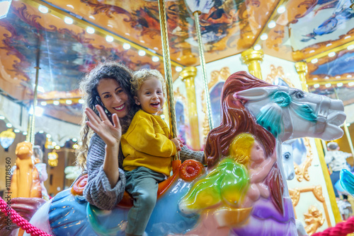 Mother and son waving while riding carousel horse at amusement park photo