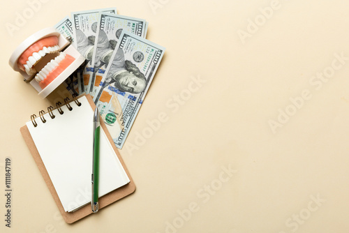 Flat lay composition with educational dental typodont model and money with notebook on colored table, top view. Expensive treatment photo