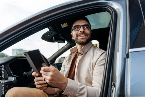 Confident Hispanic man holding digital tablet, using mobile app or navigator in modern new car