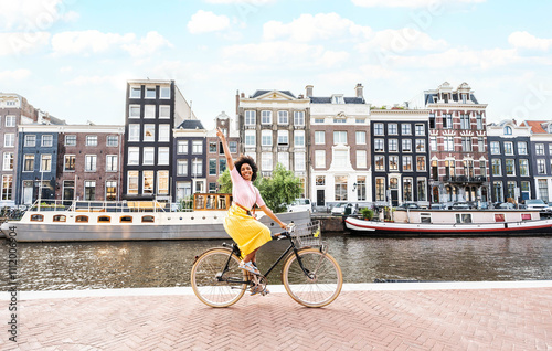 Happy female tourist visiting Amsterdam city, Netherlands - Delightful woman riding bicycle in urban street - Holidays, traveling and transportation life style concept