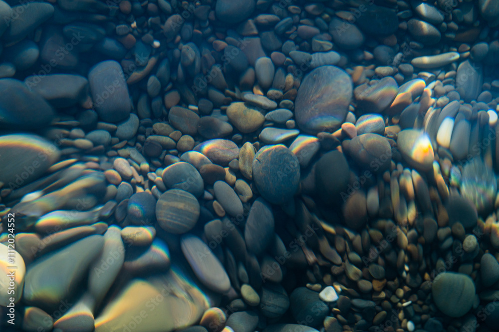 Fototapeta premium Underwater pebble backgrounds. Colorful stones sea bottom in the sun rays. View from above through clear water. Seascape wallpaper texture. Defocus.