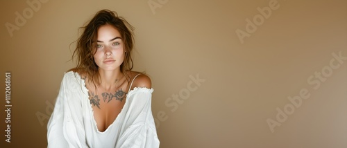 Tattooed individual with tousled hair relaxes against a neutral backdrop, capturing a moment of calm and reflection in a cozy indoor setting