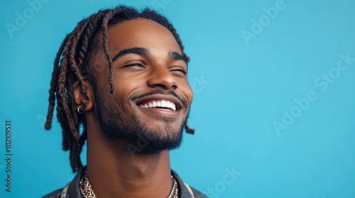 Happy ethnic man with braided hair and stylish jewelry smiling against blue background