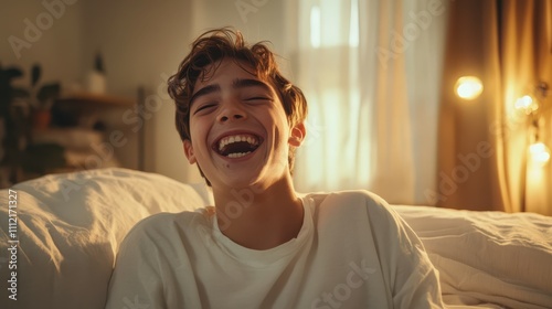 Happy teenage boy laughing near bed at home