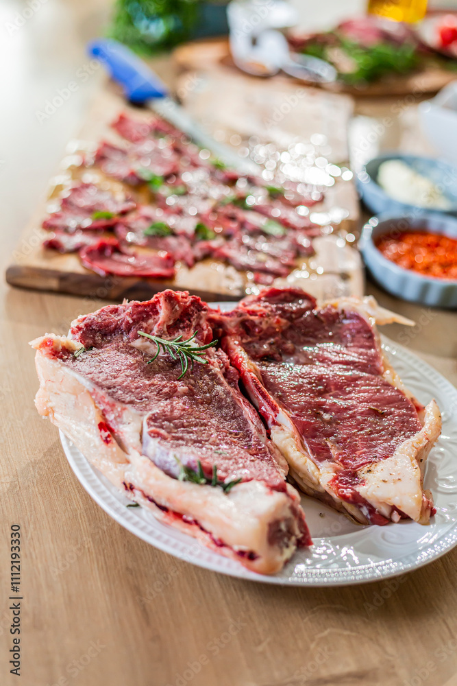 Two florentine steaks seasoned with rosemary and salt, ready to be cooked, resting on a white plate on a wooden table Two florentine steaks seasoned with rosemary and salt, ready to be cooked, resting on a white plate on a wooden table