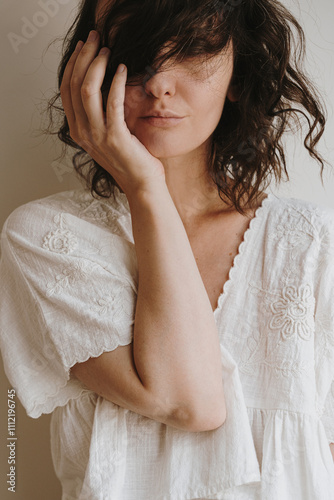 Close-up of pretty woman in white embroidered blouse with wavy messy hair framing her face in a relaxed carefree portrait