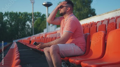 Disappointed stressed emotional fan man on tribune stadium. Lonely man fidgets on stands, supporting team outsiders. Last team of championship, lonely sad upset fan on stadium stands. Fan is worried.