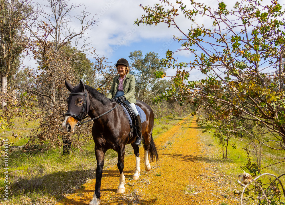Senior woman riding horses along a narrow dirt path. Senior woman riding horses along a narrow dirt path.