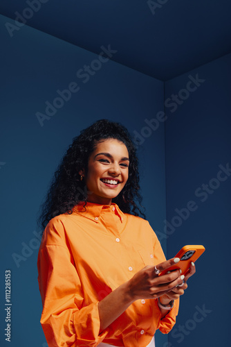 Happy woman using mobile phone in bright, colorblocked monochromatic space, portraying modern creativity