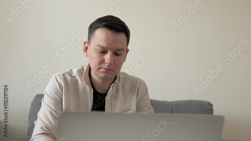 Man is using laptop texting at home on sofa. Working online, digital, IT, remote concept. Focused business man looking at computer. 