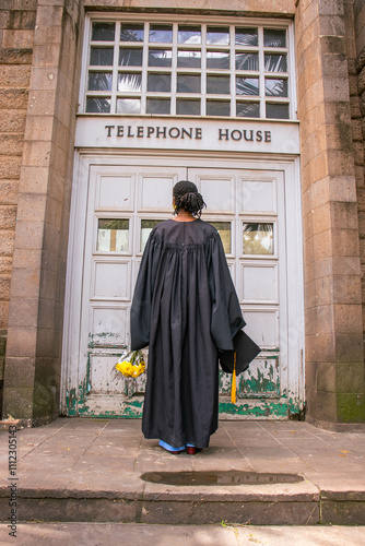 A you black woman wearing a graduation gown looking excited to be a graduand