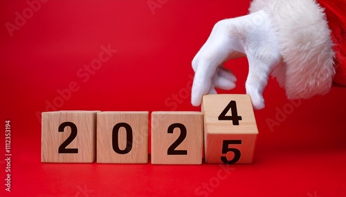 Gloved hand in Santa suit changes wooden block from 2024 to 2025 on bright red background. photo