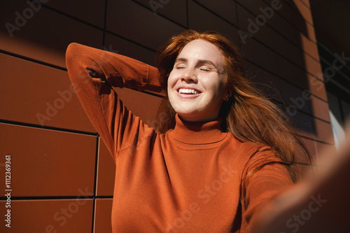 Happy young woman taking selfie in front of brown wall