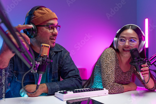 Two young asian streamer host making live podcast with condenser microphone and tablet at broadcast home studio. Content creator and social media influencer creating digital content.