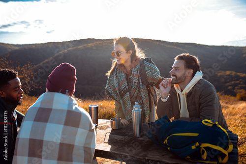 Group of friends sitting on the top of the hill at bench resting after hiking and drinking tea. photo