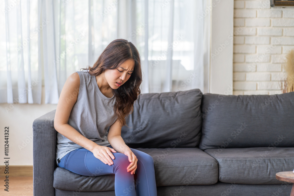 Asian woman suffering from knee pain and inflammation, arthritis symptoms sitting on sofa, health and wellness, joint pain, lifestyle health concept at home, healthcare awareness, knee problem relief Asian woman suffering from knee pain and inflammation, arthritis symptoms sitting on sofa, health and wellness, joint pain, lifestyle health concept at home, healthcare awareness, knee problem relief