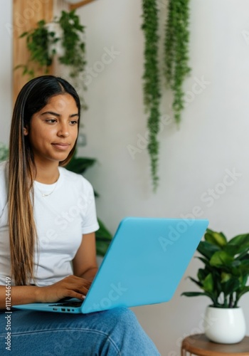 Young Hispanic woman using blue laptop in modern home office with plants