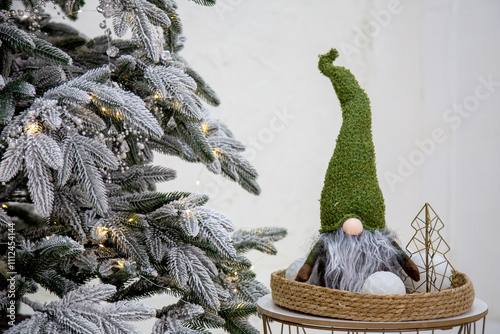 Festive holiday setup featuring a charming Christmas gnome with a green textured hat and fluffy gray beard, displayed on a woven tray with decorative snowballs and a metal wire tree.