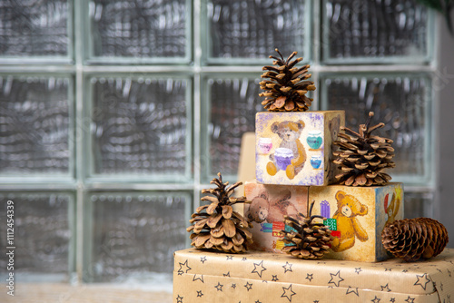 Festive composition featuring hand-painted wooden blocks with teddy bear designs, natural pinecones, and a gift box wrapped in star-patterned paper, set against a textured glass backdrop. Perfect for 